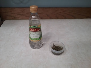 A bottle of vinegar next to a small cup containing terragon leaves soaking in vinegar.