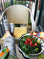 My legs crossed on a balcony chair with a salad on the table next to me.