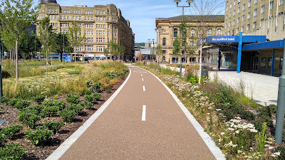 A buff two way cycle track running through a linear park full of flowers and landscaping.