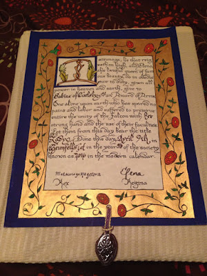 A blue-bordered medieval-style piece of paper with a wide gold inner border covered in vining red roses with green leaves, and with fancy calligraphy in the center and a small purple wax seal attached at the bottom.