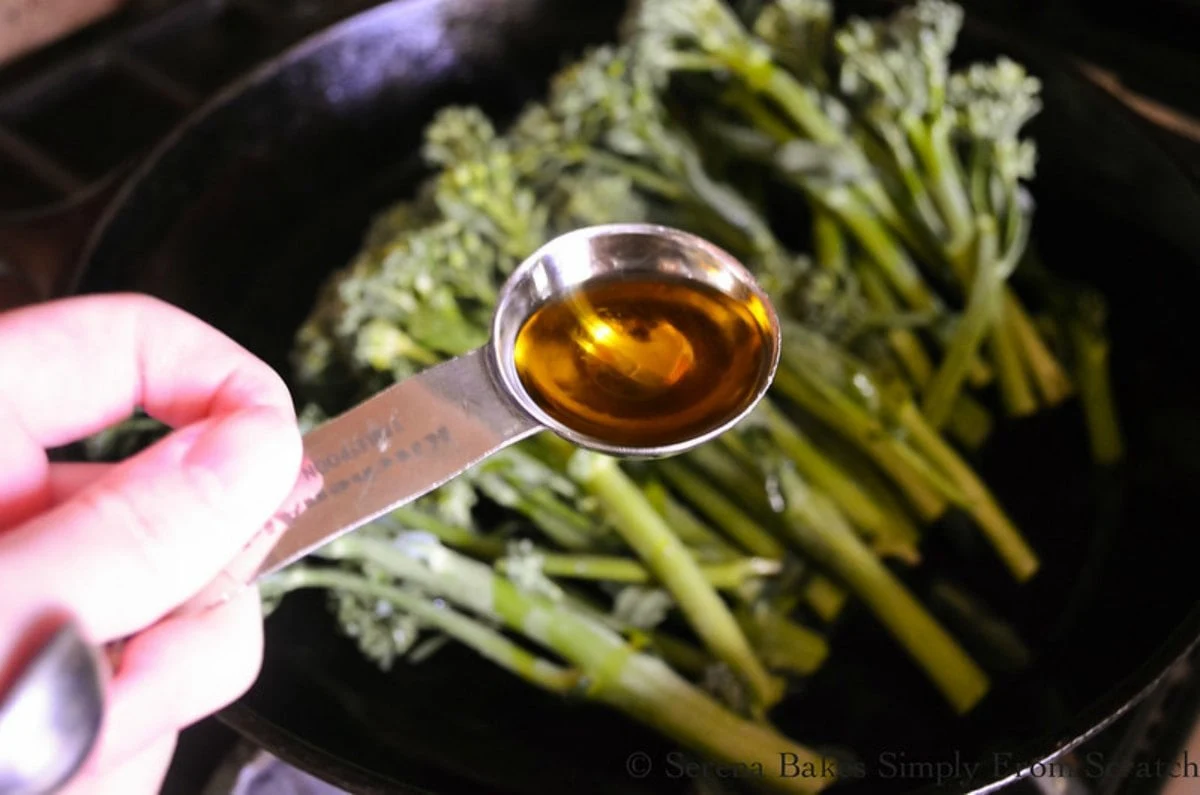 Cast Iron Skillet with Broccolini and a tablespoon filled with Olive Oil.