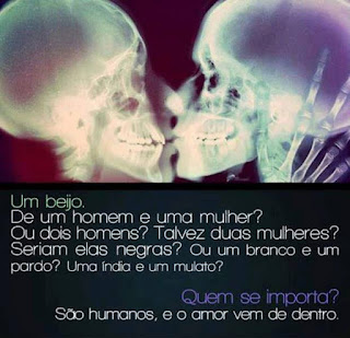 Raio X em fundo vermelho-escuro do crânio de duas pessoas. Elas estão de perfil beijando-se na boca. A da esquerda tem a mão ossuda, direita, gentilmente pousada nos ossos do rosto e crânio da outra pessoa. Abaixo em letras brancas sobre fundo preto lê-se: Um beijo. De um homem e uma mulher? Ou dois homens? Talvez duas mulheres? Seriam elas negras? Ou um branco e um pardo? Uma índia e um mulato? Quem se importa? São humanos, e o amor vem de dentro. 