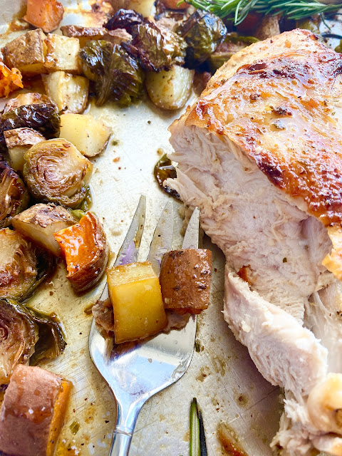 Slices of roasted turkey on a sheet pan and fork with roasted vegetables.