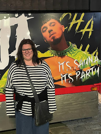 Me, looking chuffed as anything, poses infront of a poster of the Finnish singer, Käärijä outside at night.