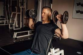 An image depicting a person doing a superset workout, which involves performing two exercises back-to-back with minimal rest in between. The person in the image is lifting weights while standing in a gym, with other gym-goers and equipment visible in the background.