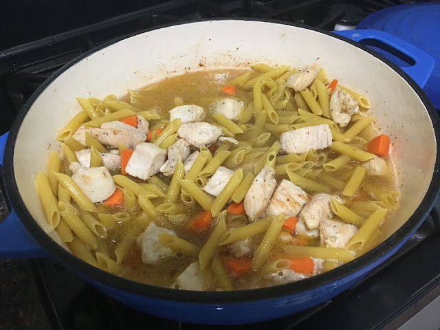 The chicken broth and water in a pan with the cooked chicken, pasta, and carrots. 