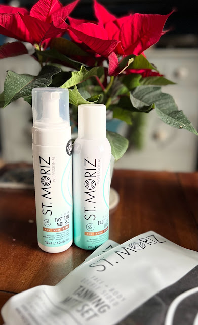 St Moriz tanning products with tanning mitts and poinsettia plants on table.