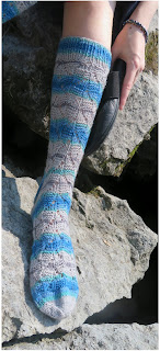 someone wearing a pair of fingering-weight socks; knit in striping yarn that goes from blue to grey. The socks have a subtle lace pattern.