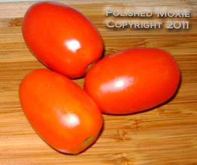 Picture of three plum tomatoes sitting on a wooden cutting board.