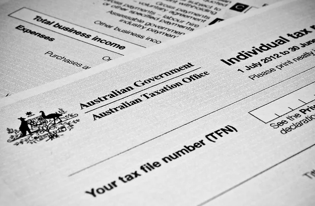 A close-up, black and white image shows sections of an "Individual tax return" form from the "Australian Government Australian Taxation Office." The form includes fields for "Total business income," "Expenses," and "Your tax file number (TFN)." The Australian Coat of Arms is visible on the left side of the form.