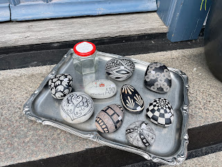 Painted rocks for sale on someones steps with a bottle to put your money in