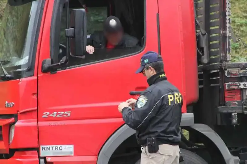 Agente da PRF conferindo documentos de um motorista de caminhão vermelho