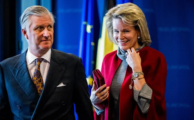 Queen Mathilde wears a black and white checked dress, with a wine-red cape coat by Natan. Diamond parrots brooch