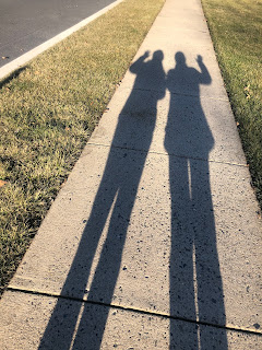 Tall shadows of me and my mom along the sidewalk, side by side like twins, waving with opposite hands.