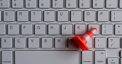 A close-up view of a white keyboard with shallow keys. A miniature traffic cone is lying across the keys.