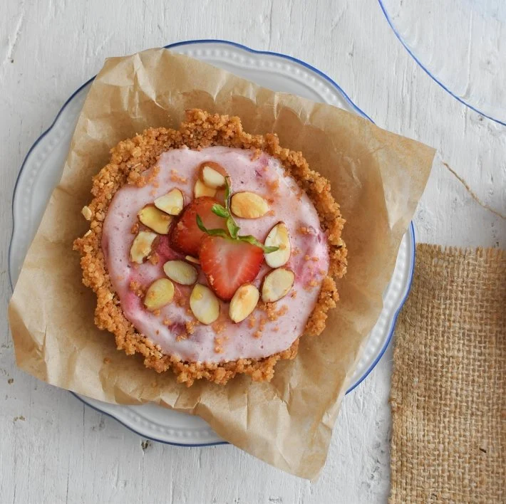 Pie de fresas con yogurt, la base se prepara con galletas de avena y se decora con almendras y fresas frescas