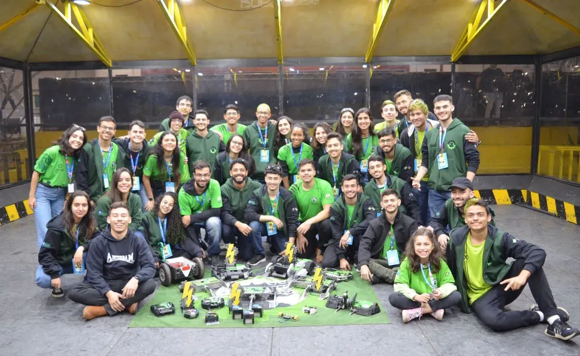 estudantes com camisetas da equipe troia posam para foto dentro de uma tenda com faixas amarelas e pretas