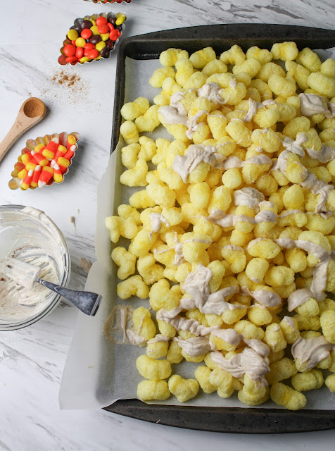 puffcorn on a baking sheet being drizzled with white chocolate.