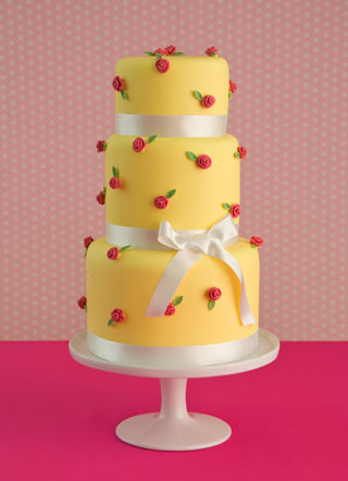 Three tier round draping wedding cake in yellow with an abundance of fresh 