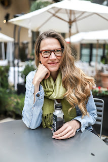 Image of a woman with long hair and glasses smiling at the camera. She is holding a soft drink in her hand. She looks at ease and comfortable in her own skin. Her names is Anna Gudmundson and she is CEO of Sensate.