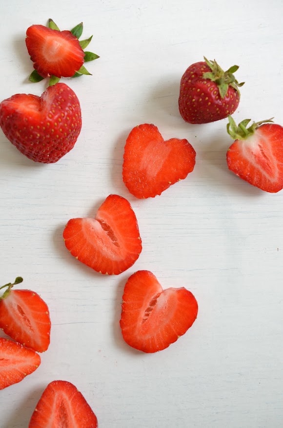 Erdbeerherzen, das sind zurecht geschnittene Erdbeerscheiben, ganze und halbe Erdbeeren liegen auf einem weißen Hintergrund.