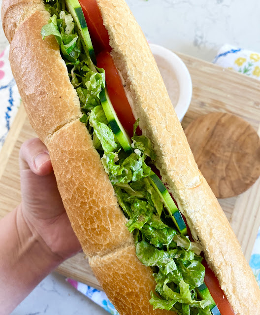 Hand holding a large sub hoagie filled with veggies.