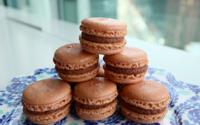 Mini pyramid of chocolate macarons sitting on a blue Anthropologie plate on a white table. 