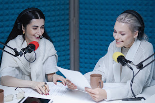 two women facing other with podcast mics.