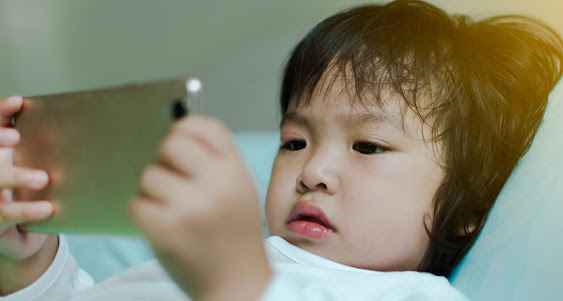 A small child playing a mobile game in bed