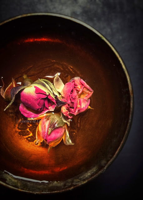 "A teapot surrounded by dried rose petals and loose tea leaves, symbolizing the process of crafting Chinese Rose Tea."