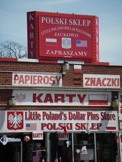 Color photo of a red and white storefront in Polish Village. The name of the shop in English is "Little Poland's Dollar Plus Store." A number of additional signs in Polish advertise the wares available within.