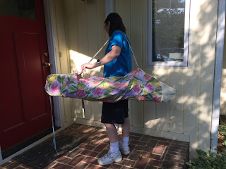 Woman carrying folding chair in homemade flowered bag with strap.