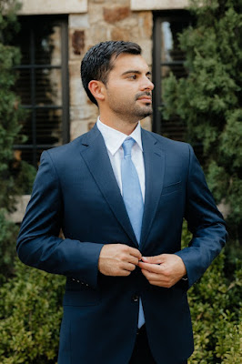 groom in navy suit with blue tie fixing jacket