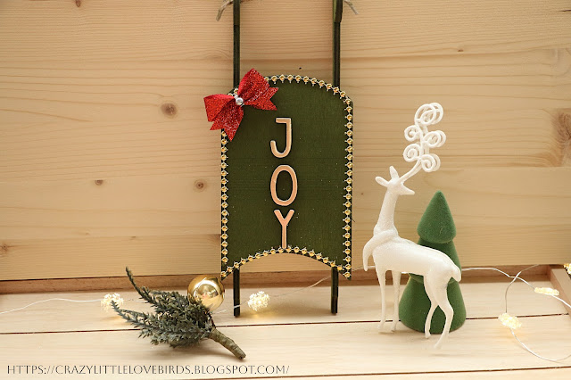 Green sled with red bow, and gold gems displayed on a wooden table