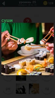 За столом палочками люди едят приготовленное суши