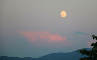 Moon rises above sunset-lit clouds