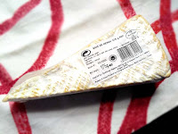 The larger wedge of Brie de Meaux, which shows the rind.