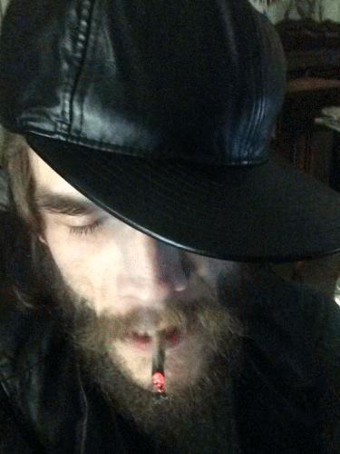 Oregonleatherballs wearing a black leather hat bearded and blowing out smoke while winking at the camera face only