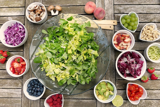 Large bowl of lettuce surrounded by several smaller bowls of assorted fruits and vegetables