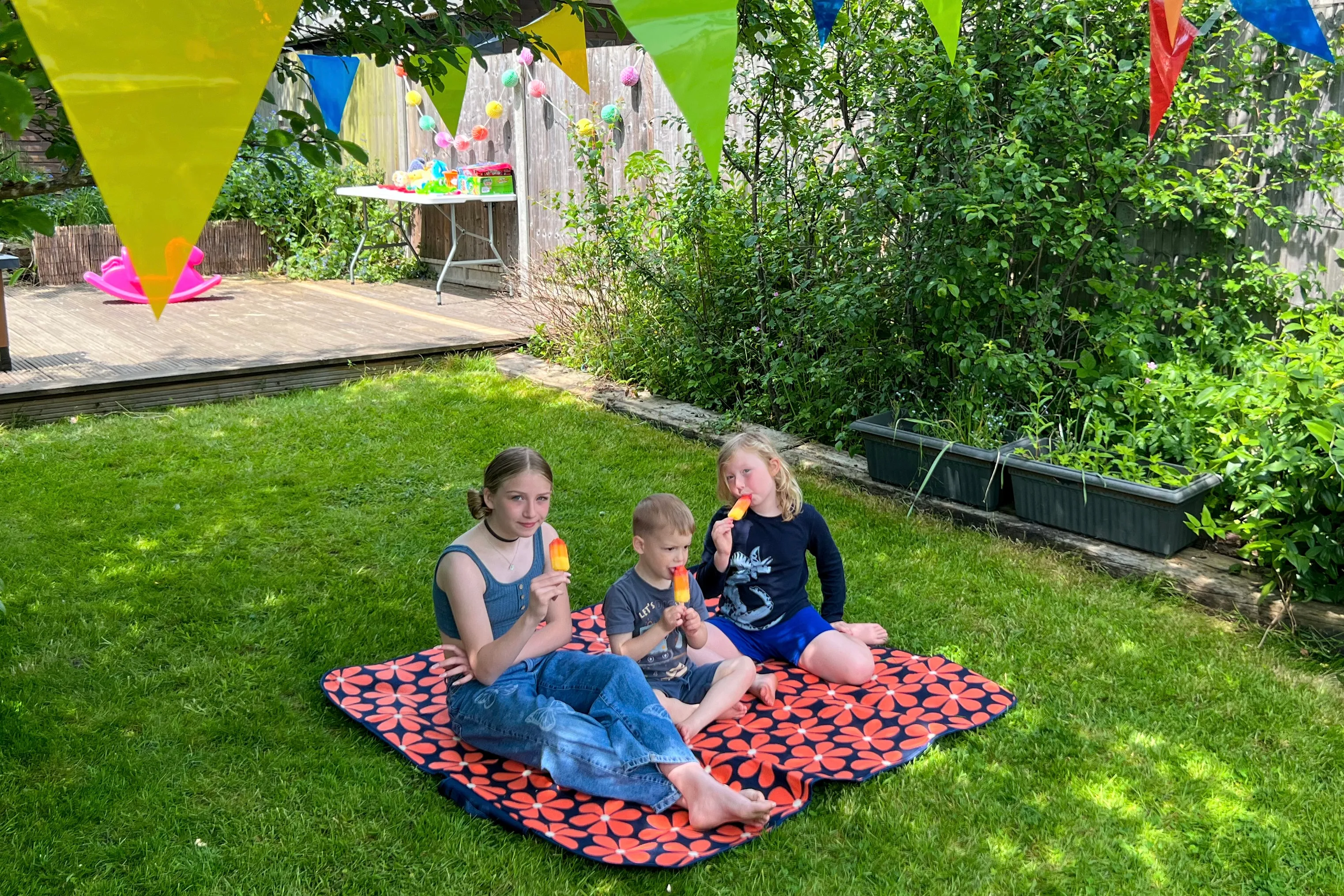 Children sitting on a picnic mat at a garden party eating ice lollies