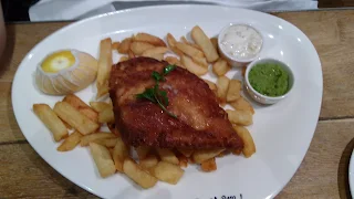 Oval white plate with large french fries and a large piece of fried fish in a deep golden brown color