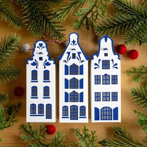 trio of blue and white Dutch-style tall house tree ornaments displayed on flat surface decorated with greenery and red felt balls