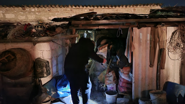 A person stepping into a rustic, overfilled storage shed at night with minimal lighting.