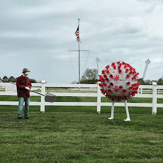 Sculpture of person in field facing large SARS-CoV-2 sculpture.