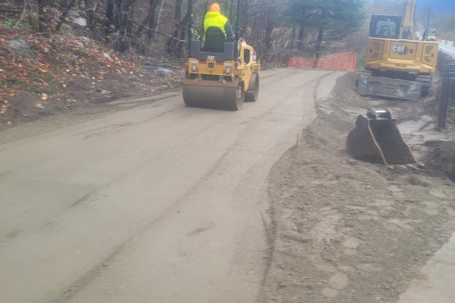 A worker on a roller compacting a pile of dirt along US 2 near Skykomish. An excavator sits along the berm next to the guardrail.