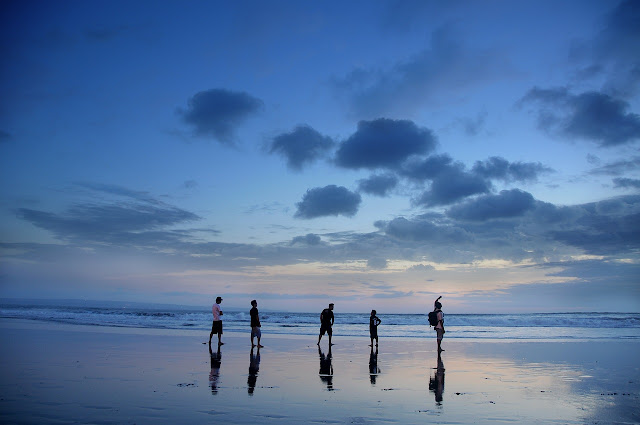 Un gruppo di persone è in piedi in spiaggia davanti al mare alla luce blu del crepuscolo