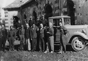 A photograph of a group of men standing together outside in front of a car. The words "Red Cross" are visible on the door.