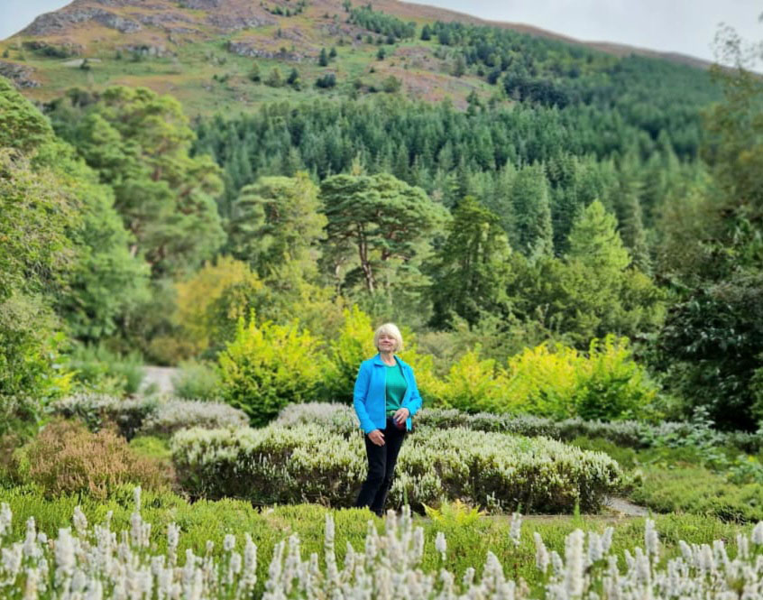 Gail Hanlon from Is This Mutton with background of woodland and fells in the Lake District