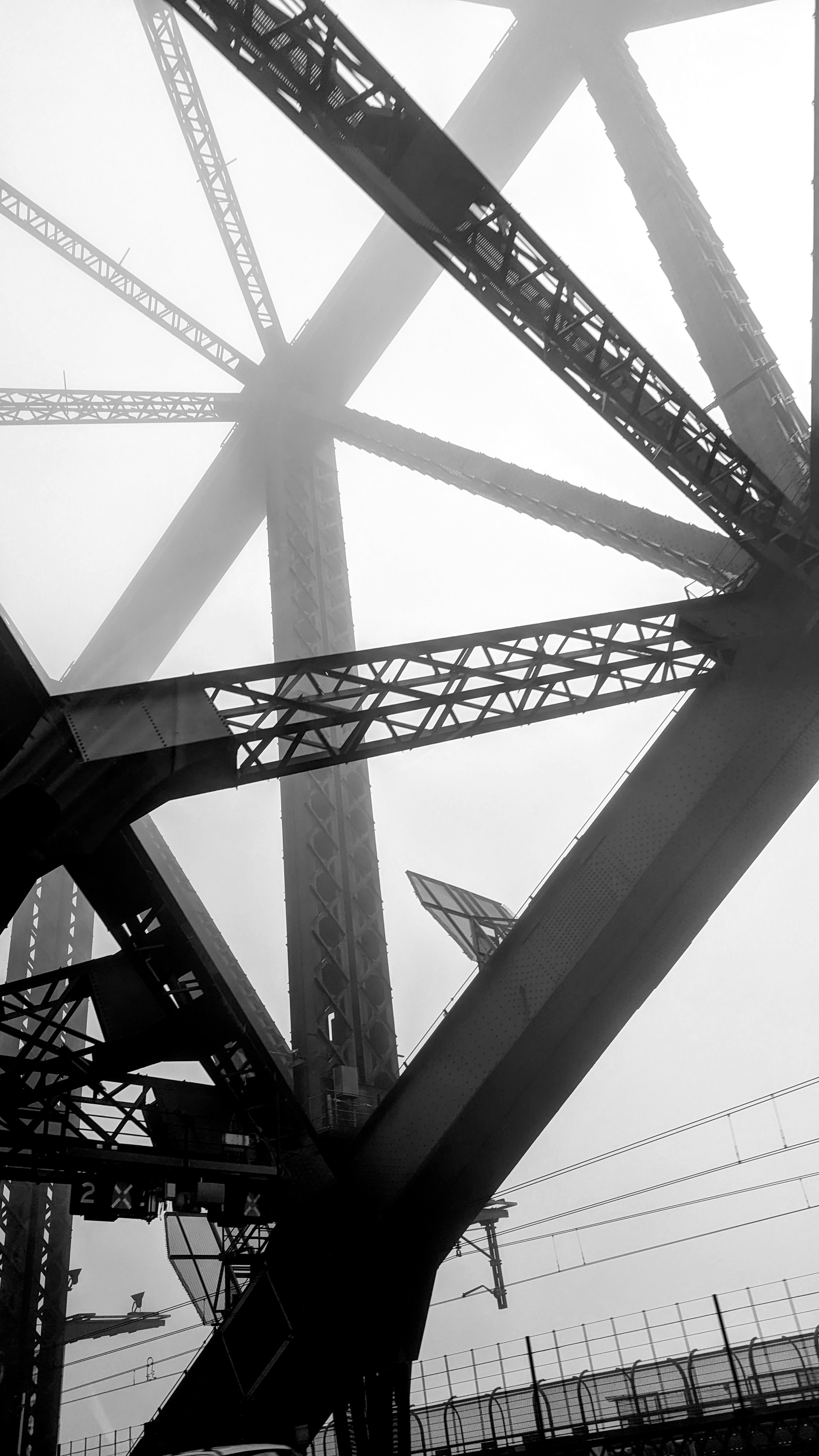 Monochrome photo showing parts of the Sydney Harbour Bridge iron structure in a foggy morning as seen from a cab driving over