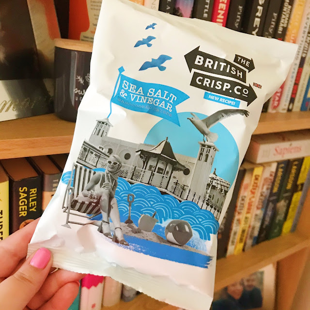 Sea salt and cider vinegar crisps held up in front of bookshelf